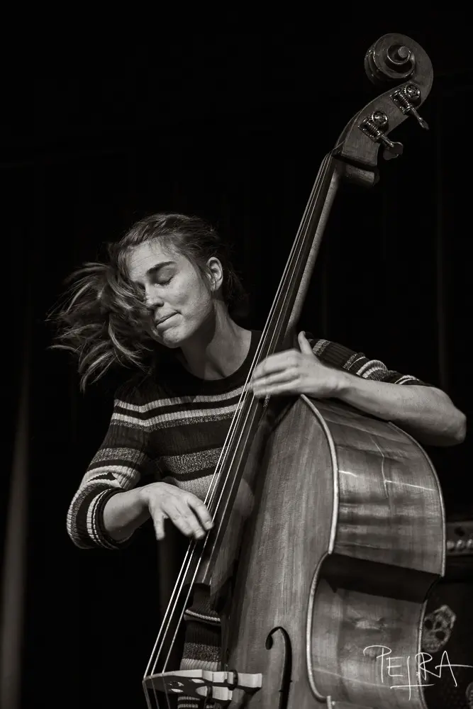 A person passionately playing an upright bass with eyes closed and hair moving, wearing a striped sweater.
