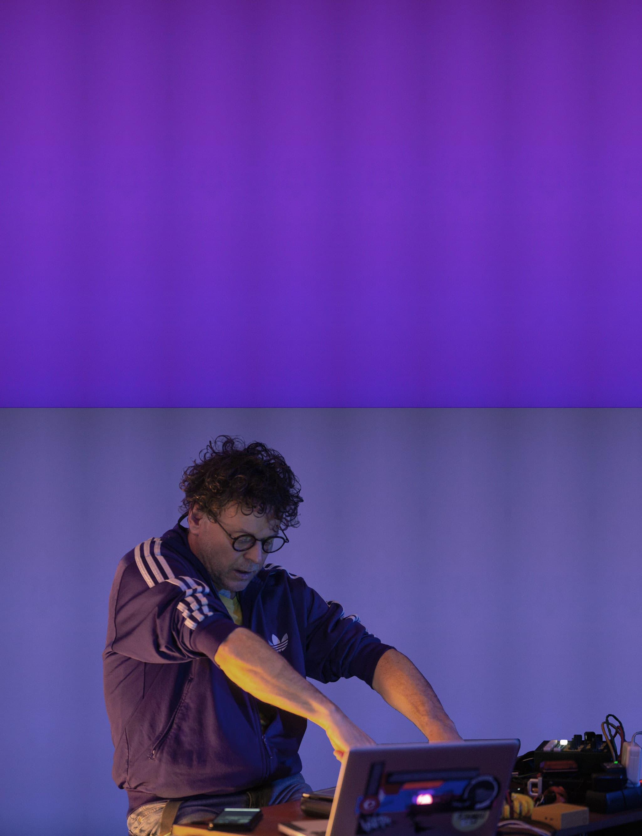 A person with curly hair and glasses is using a laptop, set against a backdrop of blue and purple lighting.