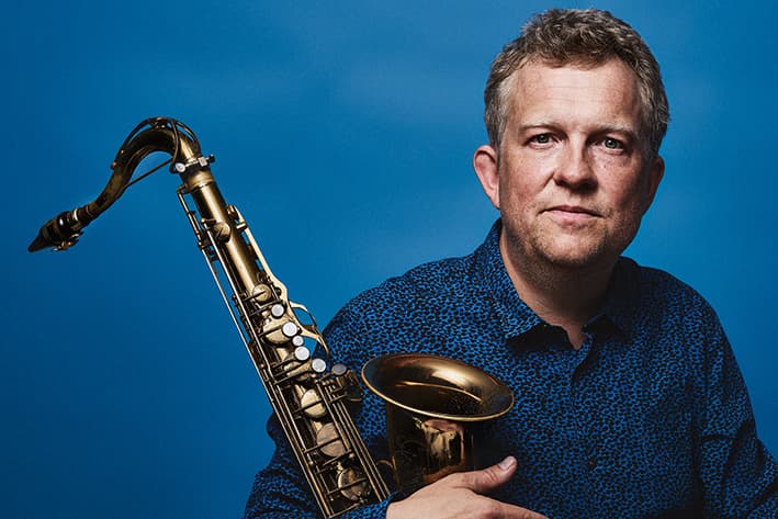 A person holding a saxophone against a blue background.