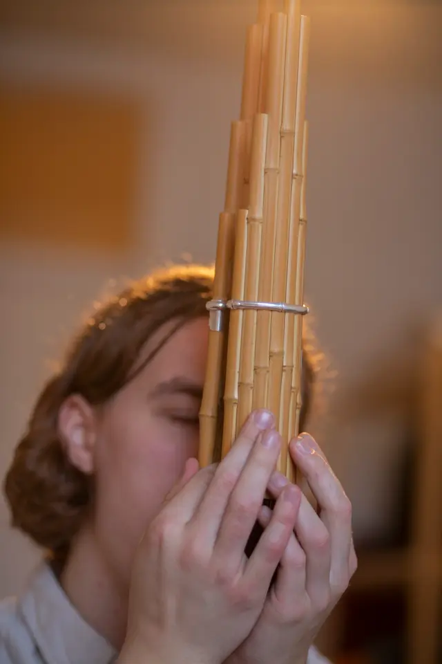 A person is playing a wooden pan flute, holding it close to their face.