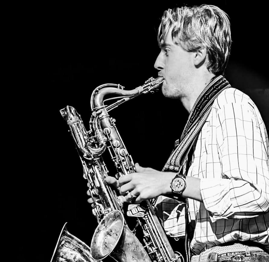 A person is playing two saxophones at the same time, captured in a black and white photo.