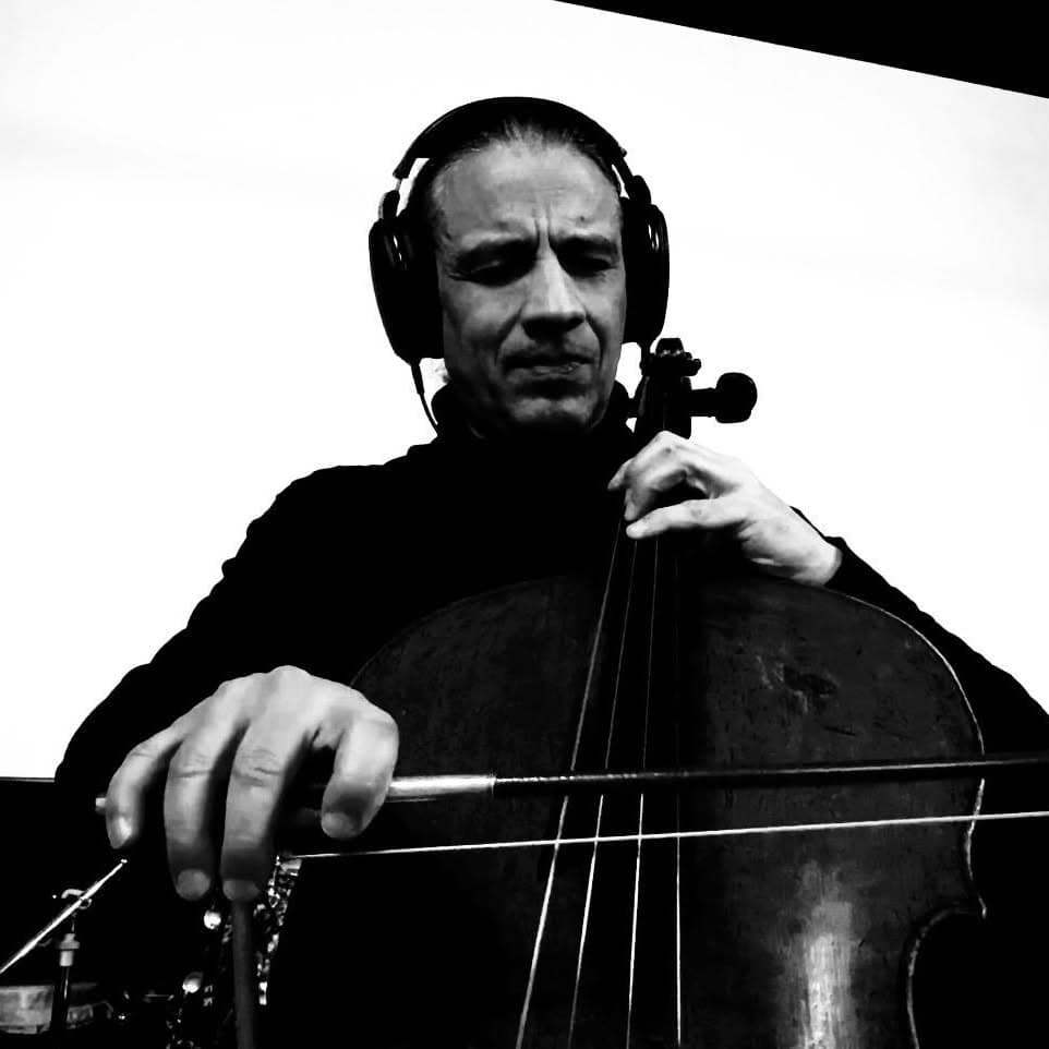 A person wearing headphones is playing a cello with a focused expression.