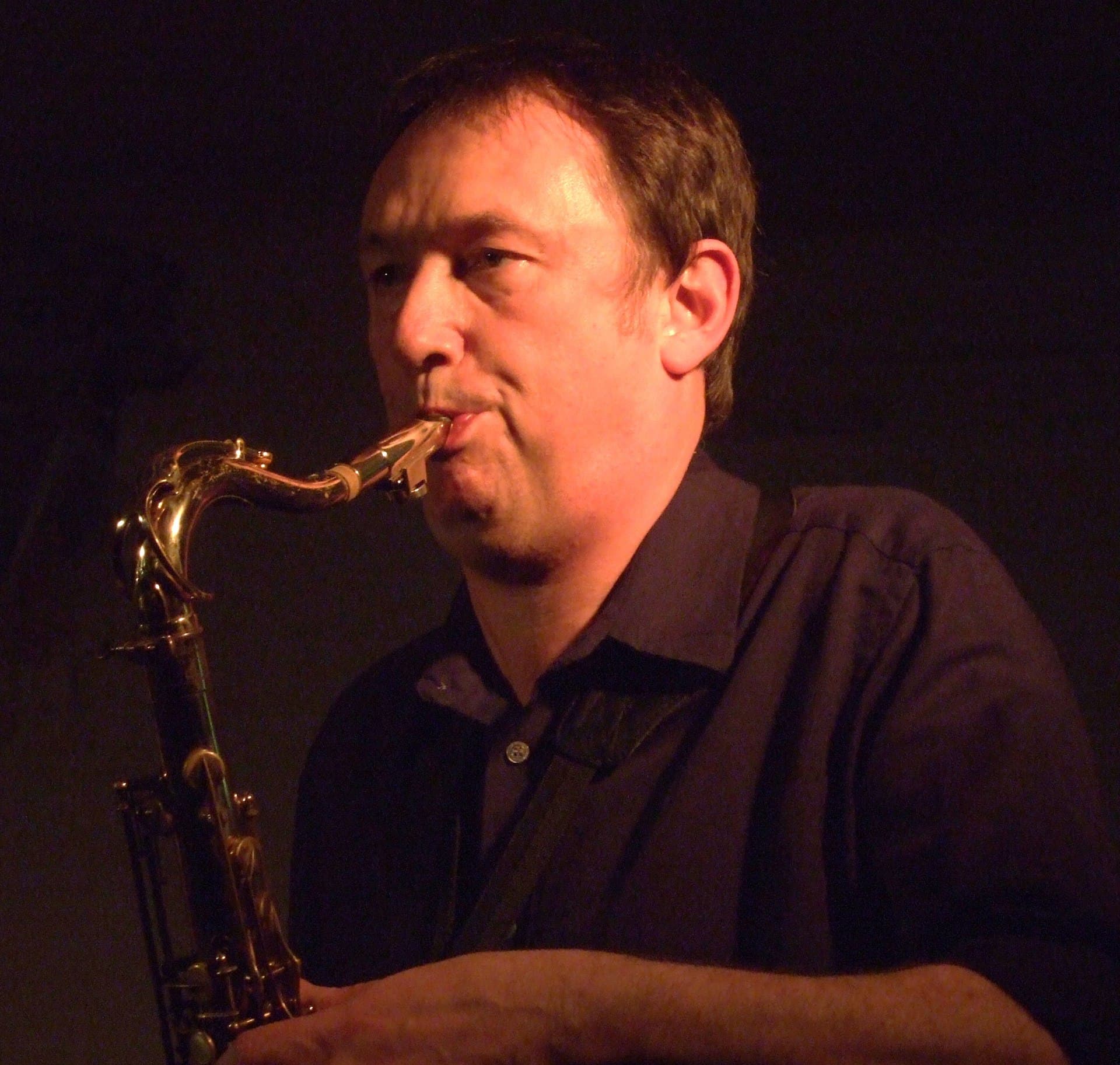 A person is playing a saxophone in a dimly lit setting.
