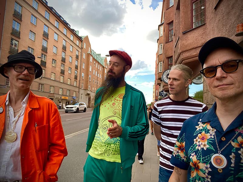 Four men in colorful outfits walk along a city street with buildings in the background.