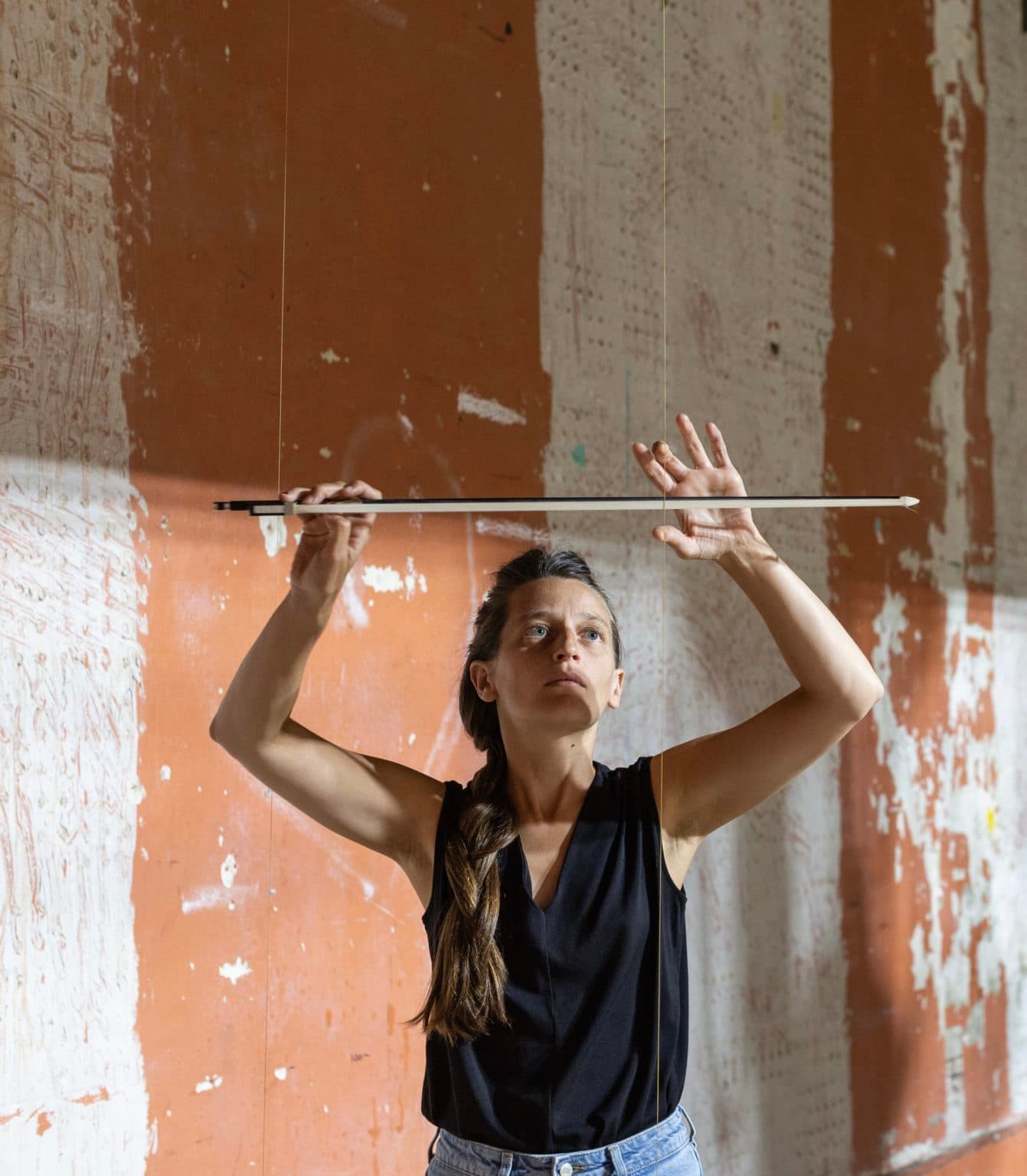 A person is adjusting a suspended horizontal rod against a textured wall.