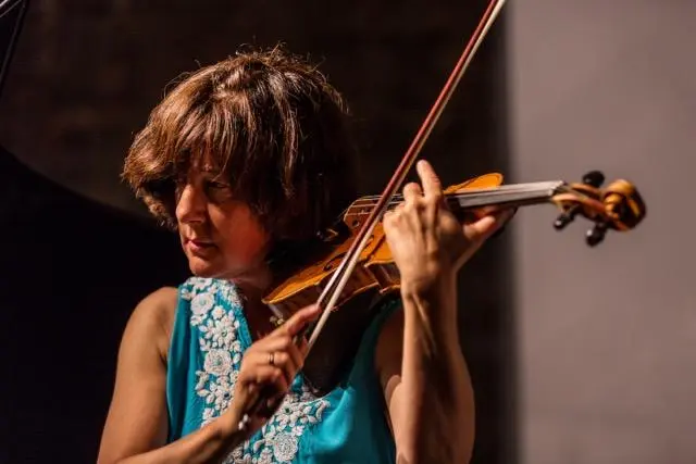 A person is playing a violin, wearing a sleeveless blue top with intricate white embroidery.