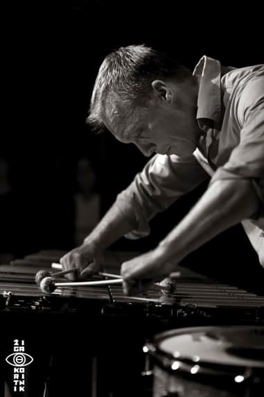A focused musician playing a vibraphone with mallets in a dimly lit setting.