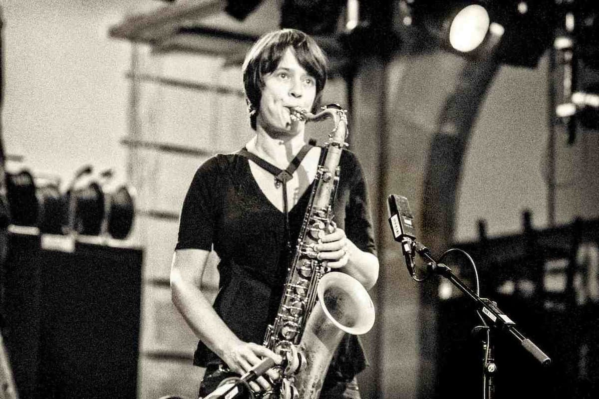 A person is playing a saxophone on stage in a black and white setting.
