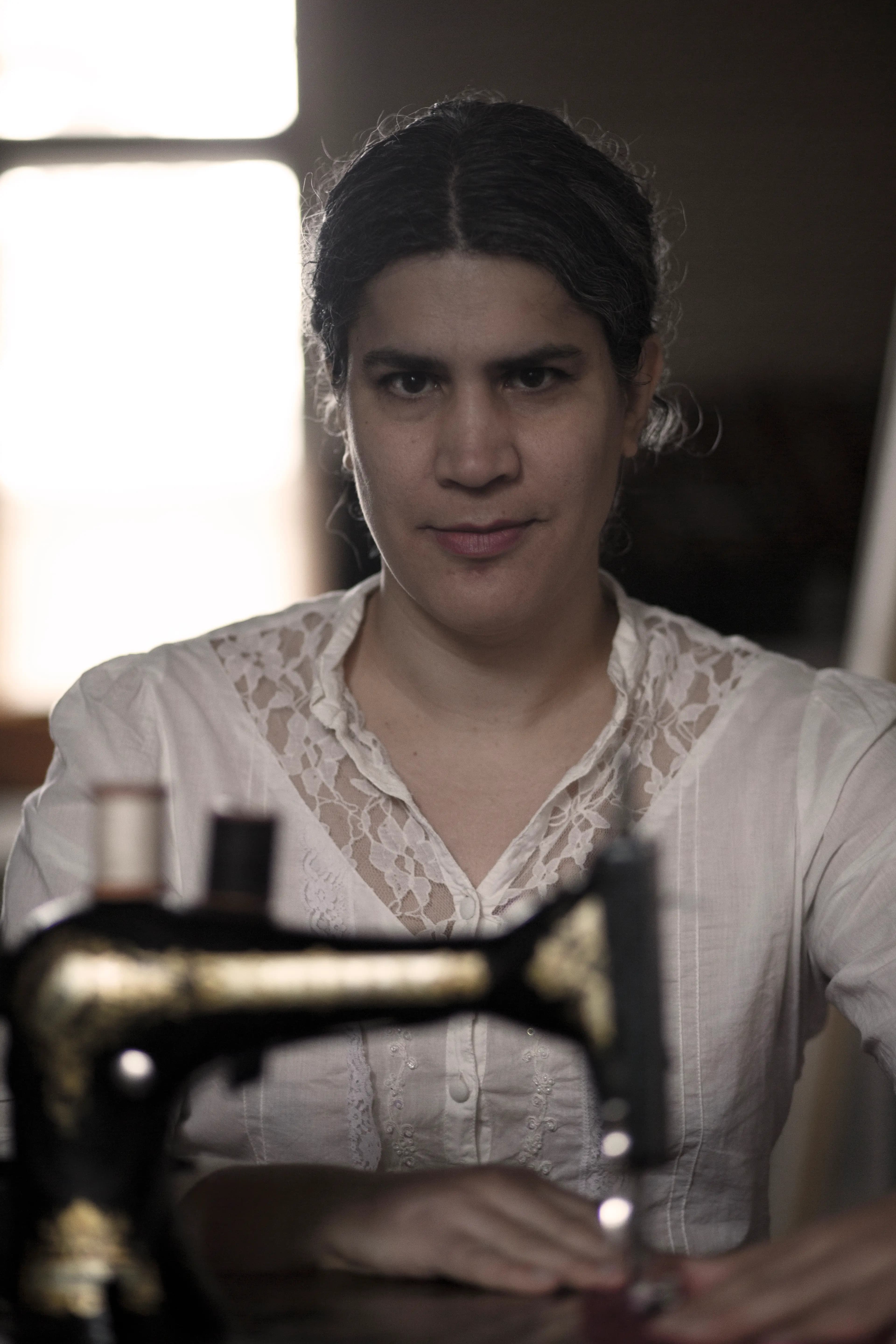 A person wearing a white lace blouse sits behind an antique sewing machine.