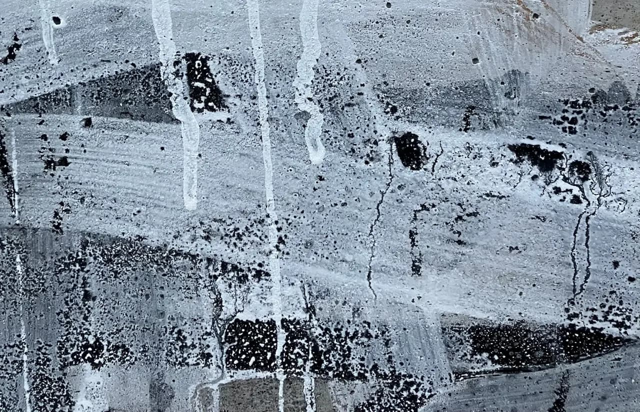 A textured abstract painting with white and black splatters and drips on a gray background.