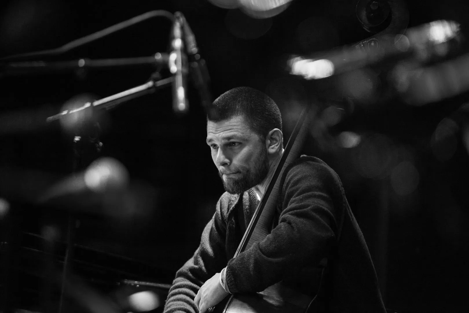 A man is playing a double bass with microphones and blurred lights in the background.