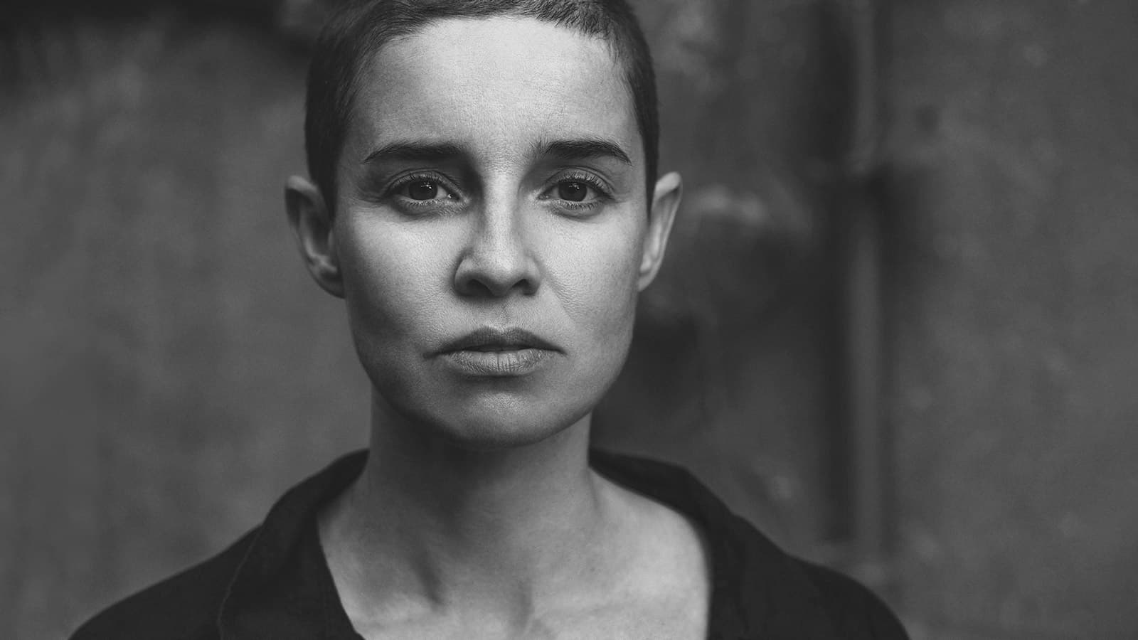 A person with short hair looks directly at the camera in a black and white portrait.