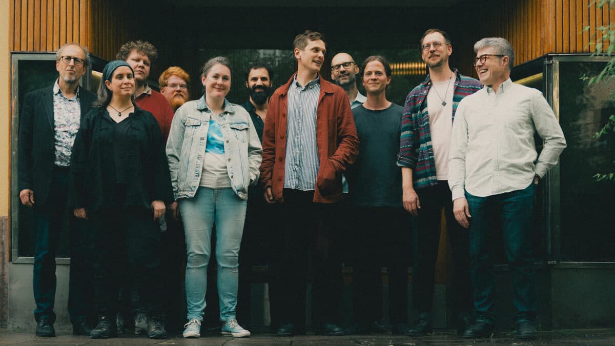 A group of eleven people are standing together, smiling, in front of a wooden building entrance.