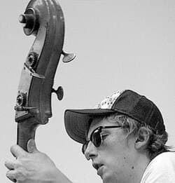 A person wearing sunglasses and a cap is playing a string instrument.