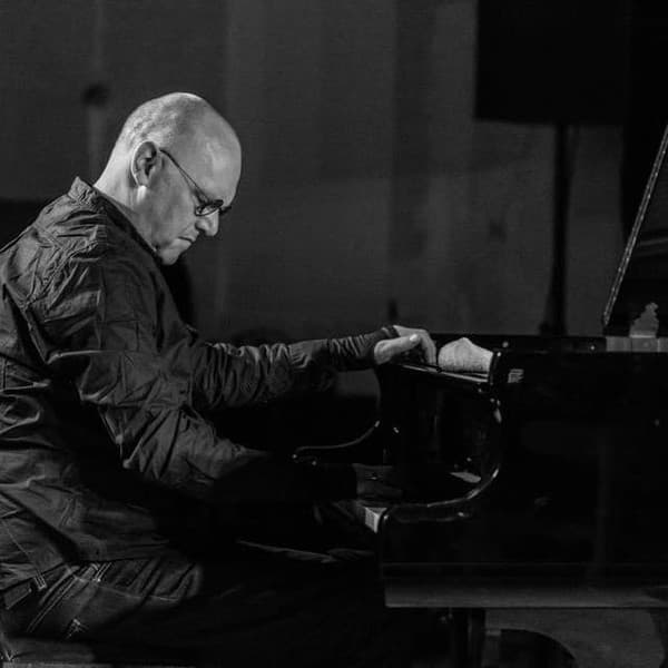 A person is playing a grand piano, focused on the keys, in a dimly lit setting.