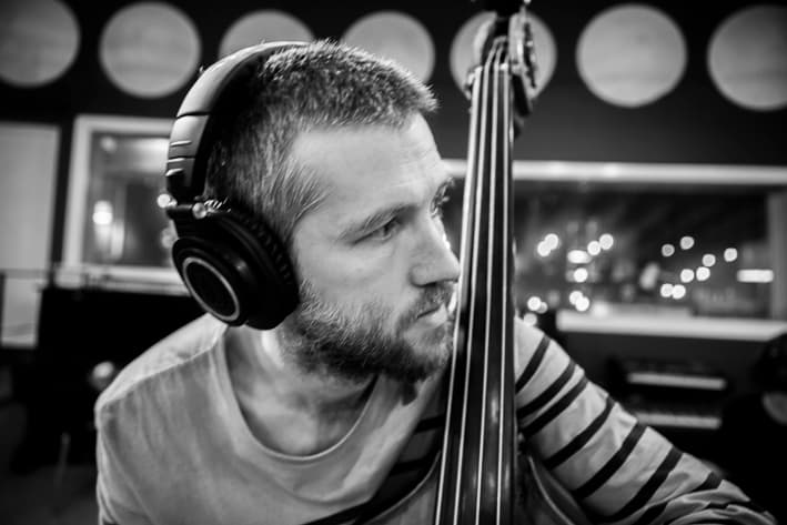 A man wearing headphones is playing an upright bass in a recording studio.