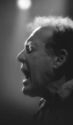 A black and white photo of a person with an expressive face, seemingly shouting, in profile view.