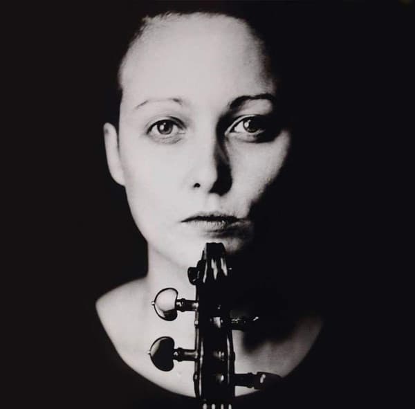 A black and white portrait of a person with a violin's scroll in front of their face, creating a symmetrical composition.